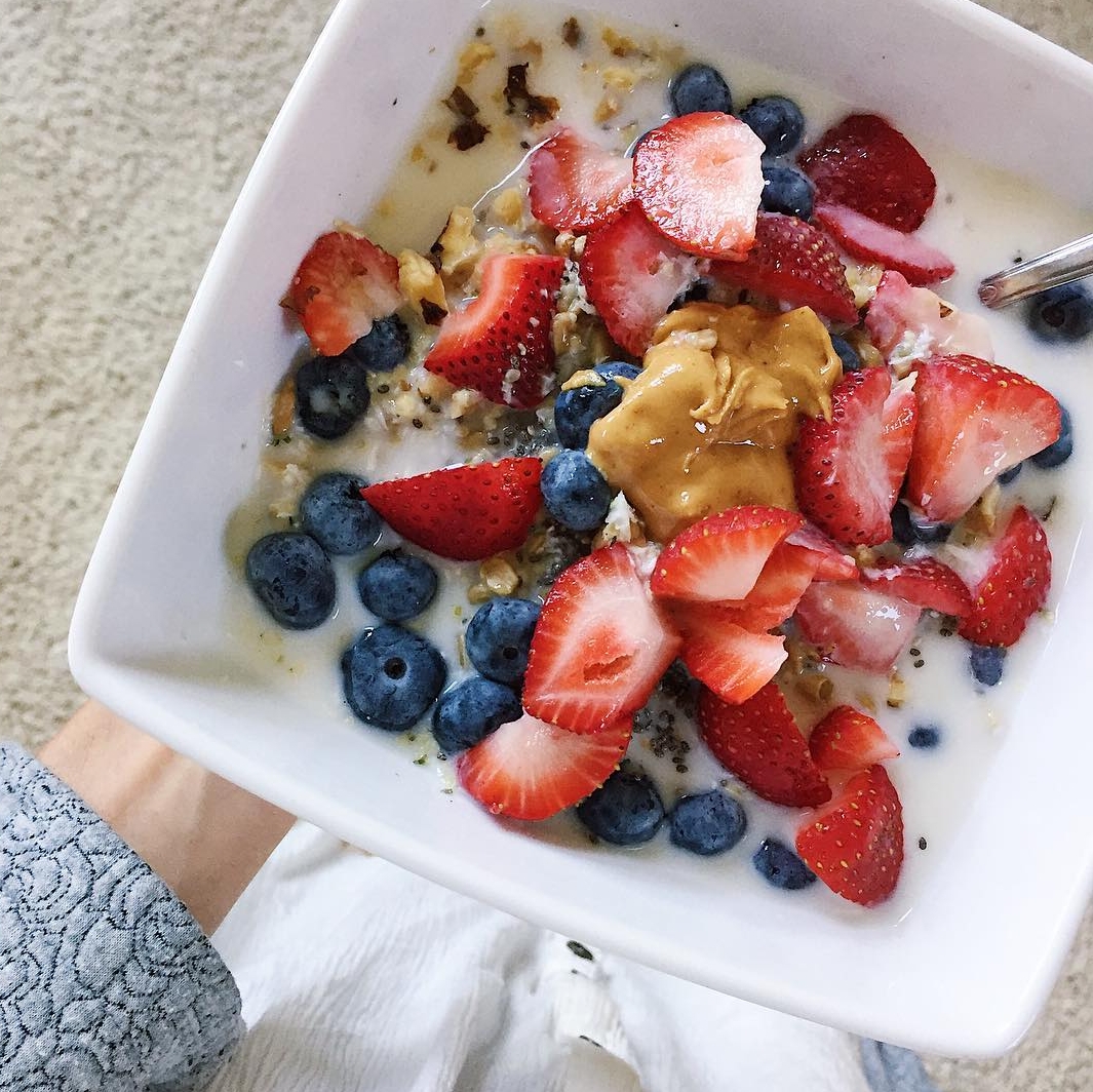 A bowl of oatmeal with strawberries, blueberries, and peanut butter.